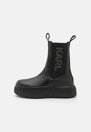 Sort Chelsea-støvle med plateau og rillet sål, elastisk sidepanel mærket "KARL" med nitter samt trækflapper foran og bagpå.