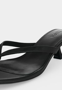 Μαύρο δερμάτινο σανδάλι με τακούνι, λεπτά σταυρωτά λουράκια και τετράγωνη μύτη σε λευκό φόντο.