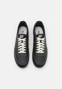 Ett par svarta Nike-sneakers med vita snören och synlig Nike-logotyp på tungan, visade på en plain vit bakgrund.