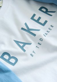 Biały i jasnoniebieski materiał z wypukłymi, morskozielonymi literami tworzącymi napis „BAKER BY TED BAKER” na ubraniu.