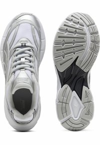 Des chaussures de sport Puma avec une tige en mesh blanc, des accents gris texturés et une semelle extérieure en caoutchouc noir et blanc flexible avec des motifs de traction.