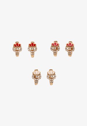 Deux paires de bagues en or avec émail rouge et cristaux, et une paire avec émail blanc et cristaux, disposées sur un fond blanc.