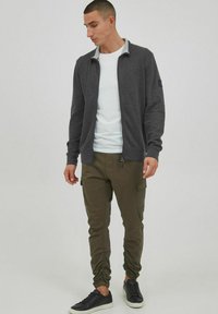 Gray zip-up jacket with a contrasting collar, paired with olive cargo pants. Black sneakers complete the outfit, emphasizing casual comfort.
