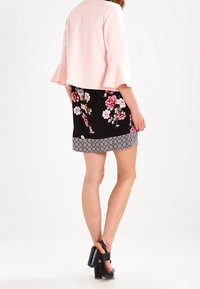 Jasnoróżowy krótki top z dzwonowymi rękawami, w połączeniu z czarną spódnicą w kwiaty z różami w odcieniach różu i bieli oraz wzorzystym hemem. Czarne sandały na obcasie.