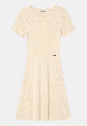 Beżowa prążkowana sukienka dzianinowa z krótkimi rękawami, okrągłym dekoltem, rozkloszowaną spódnicą oraz ozdobnymi skrzyżowanymi wzorami na przednim panelu.