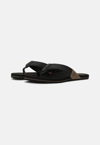 Black flip-flops with synthetic straps, featuring a textured design and a contrasting beige accent on the heel. Flat sole with slight curvature.
