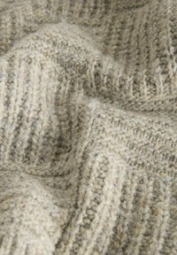 Miękka, beżowa tkanina wełniana o teksturowanym, dzianinowym wzorze, z pionowym prążkowaniem i subtelnymi wariacjami grubości włókien.