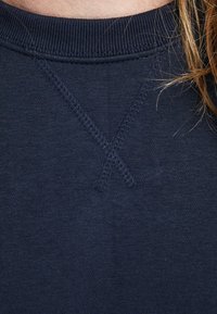Tissu de sweat-shirt bleu marine avec une texture douce, présentant un accent de broderie en croix au niveau du col et un col côtelé.