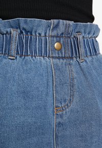 Jeansshorts med en rynkad midja och en framknapp. Ljusblå färg med orange sömmar och en slät textur. Två sidfickor.