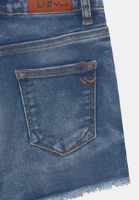 Shorts in denim bluastro con orlo sfilacciato. Presentano una tasca posteriore con cuciture a contrasto e un'etichetta in pelle sulla vita.