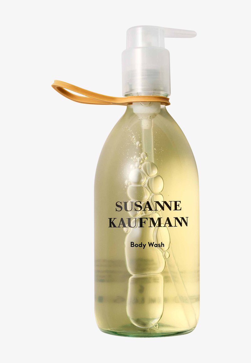 Flacon-pompe transparent de gel douche Susanne Kaufman jaune clair avec une boucle en silicone beige attachée au col.