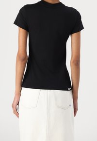 Svart kortärmad t-shirt med klassisk rund halsringning, tillverkad av ett mjukt tyg, uppvisad mot en ljus bakgrund, tillsammans med en vit kjol.