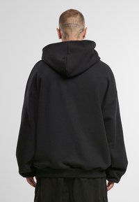 Felpa oversize nera con cappuccio ampio, polsini e orlo a coste. Realizzata in tessuto morbido, presenta una superficie liscia e una vestibilità comoda.