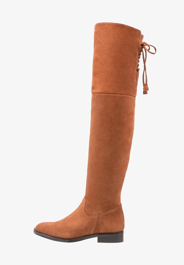 Hohe braune Wildlederstiefel mit einem taillierten Design, flacher Sohle und einem Schnürdetail auf der Rückseite. Die glatte Textur verbessert das Gesamtbild.