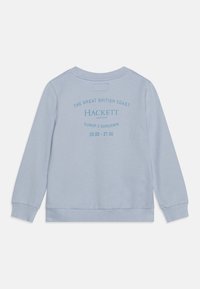 Sudadera azul claro con cuello redondo, puños y dobladillo acanalados. Presenta texto impreso en la parte posterior, incluyendo "Hackett" y una referencia temporal.