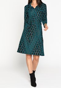 Svart klänning med turkos diamantruta, långa ärmar, krage, bälte i midjan och knälång kjol.