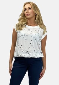 Biała bluzka z czarnym falistym wzorem, krótki rękaw i zbierany dół, zestawiona z granatowymi spodniami. Gładka tekstura, casualowy design.