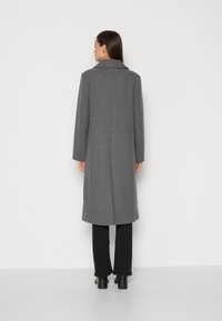 Grå ullfrakk med et enkelt design, stor krage og lange ermer, som faller under kneet. Glatt tekstur, minimal detaljering, ingen synlige lukkinger.