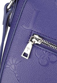 Borsa in pelle viola con superficie texturizzata, dotata di accessori in argento e chiusura con zip. I dettagli distintivi includono design in rilievo e un'etichetta con logo.