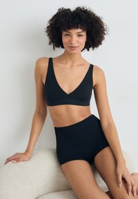 Schwarzer Bralette mit tiefem V-Ausschnitt und weichem Stoff, kombiniert mit hochgeschnittenen schwarzen Panties. Beide Teile haben eine glatte Textur.
