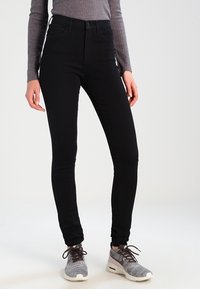 Black skinny jeans with a high waist, made of stretchy denim; paired with grey athletic sneakers featuring textured detailing.