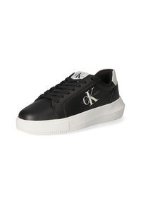 Sneakers in pelle nera con suola in gomma bianca, caratterizzati da un logo prominente, lacci neri e un accento sul tallone bianco in contrasto.