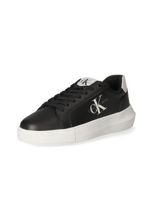 Sneakers in pelle nera con suola in gomma bianca, caratterizzati da un logo prominente, lacci neri e un accento sul tallone bianco in contrasto.