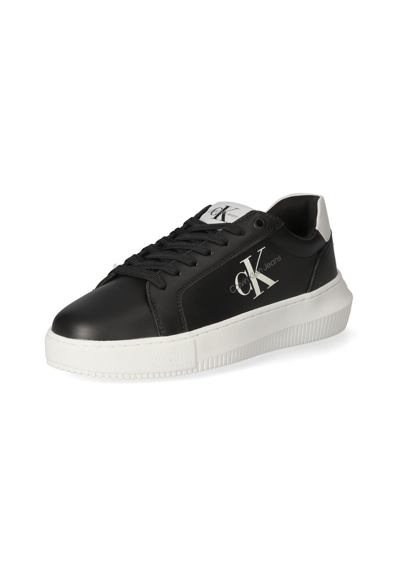 Sneakers in pelle nera con suola in gomma bianca, caratterizzati da un logo prominente, lacci neri e un accento sul tallone bianco in contrasto.