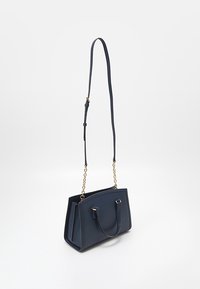 Sac à main rectangulaire bleu foncé avec des poignées courtes et une longue bandoulière ajustable ornée de maillons en chaîne dorés sur un fond uni.