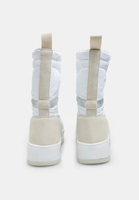 Witte en beige high-top sneakers met een gewatteerd ontwerp, voorzien van suède accenten en een gestructureerde rubberen zool. De achterkant toont elastische banden.