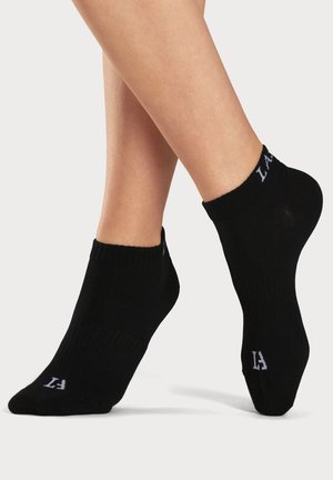 Schwarze Knöchelsocken aus weichem Stoff, mit geripptem Design und weißem Logo-Detail am Bund. Körpernaher Schnitt.