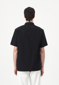 Maglietta nera a maniche corte con texture a righe verticali, colletto e taglio dritto, con dettagli di cucitura sottili sulle spalle e sulla schiena.
