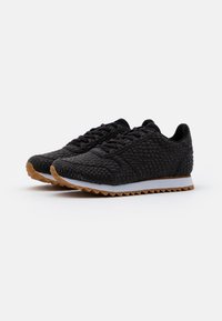 Black textured sneakers with a patterned upper, lace-up design, white midsole, and gum rubber sole featuring a triangular tread pattern.