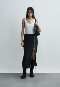 Svart maxikjol med dragkedja och framslits, kombinerad med ett vitt linne och svarta ankelboots, accessoriserad med en liten svart väska.