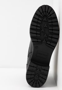 Černá bota s texturovanou gumovou podešví a robustním vzorem, hladkým svrškem a embosovaným logem značky.