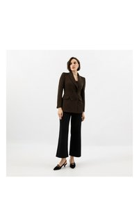 Hnědý dvouřadý blazer s vycpávkami v ramenech, kombinovaný s černými širokými kalhotami a podpatky. Hladká textura, klasický design, funkční kapsy.