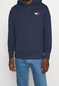 Sudadera azul marino hecha de una mezcla de algodón, con un bolsillo frontal y un parche con el logo. Tiene capucha con cordón y puños acanalados.