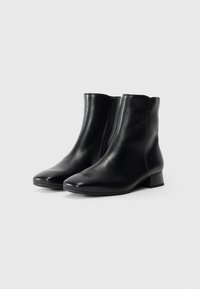 Par de botas de tobillo de cuero negro con cremallera lateral y tacón bajo sobre fondo blanco liso.