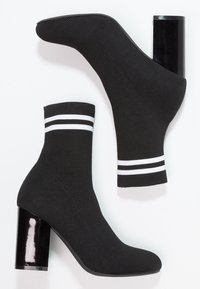 Bottines en tricot noires à bout rond, avec un revers rayé blanc et un talon carré noir brillant. Tissu texturé et éléments de design modernes.