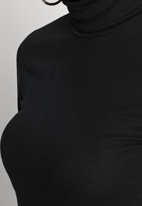 Schwarzes geripptes Rollkragenshirt mit körpernahem Design. Der Stoff ist glatt und elastisch und verfügt über einen hohen Kragen sowie Seitennähte.