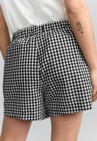 Shorts à carreaux noir et blanc avec une taille élastique, présentant un tissu texturé et une coupe ample, visibles de l'arrière.
