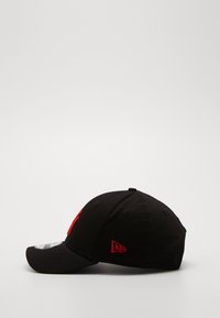 Chapéu preto com uma aba curvada, apresentando um logótipo vermelho proeminente na frente e um pequeno emblema vermelho de lado, feito de tecido texturizado.