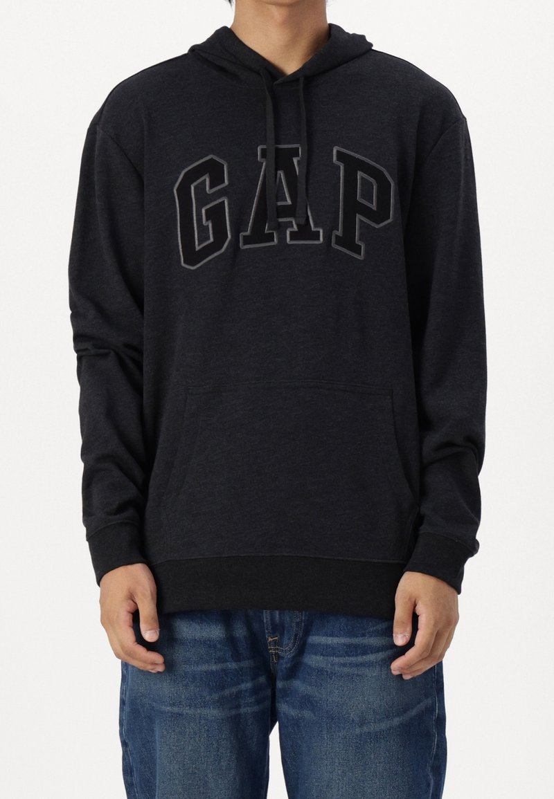 Sudadera con capucha negra que presenta un gran logo "GAP" en gris oscuro. Tejido suave, mangas largas y bolsillo canguro en la parte frontal.