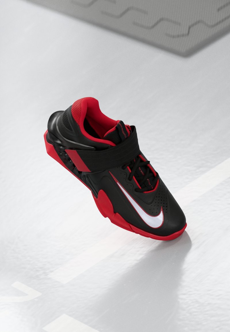 Black and red athletic shoe with mesh upper, rubber sole, Velcro strap, prominent white swoosh, and perforated toe for ventilation.