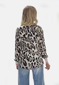 Bluse mit Leopardenmuster in Hellbeige und Schwarz, mit langen Ärmeln und gestreiften Akzenten. Glatter Stoff mit leicht tailliertem Schnitt.