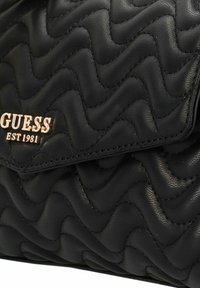 Bolso de mano de cuero negro acolchado con una textura ondulada, logo de hardware en oro y una solapa con cierre magnético.