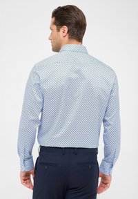 Camicia azzurro chiaro a fantasia con colletto button-down, caratterizzata da un design geometrico e maniche lunghe. Indossata con pantaloni blu navy.