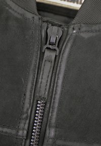 Schwarze Lederjacke mit einem auffälligen Frontreißverschluss, glatter Textur und dezenten Nähdetails entlang der Nähte.