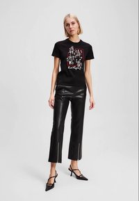 T-shirt gráfico preto com um estampado detalhado e mangas curtas, combinado com calças de pele sintética pretas com zíperes laterais e saltos agulha.