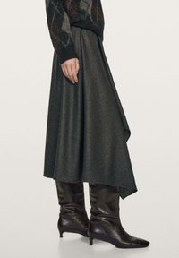 Gonna grigia scura al ginocchio con orlo asimmetrico e tessuto leggero, abbinata a stivali neri lucidi al ginocchio con punta affilata.